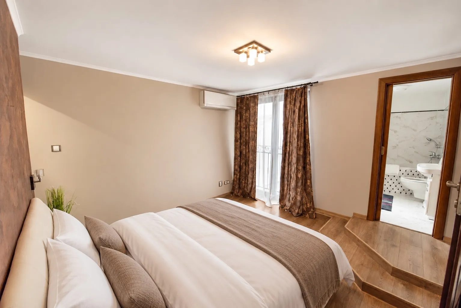 Master bedroom with a king bed, a French window with curtains, air conditioning and the en-suite door two steps up